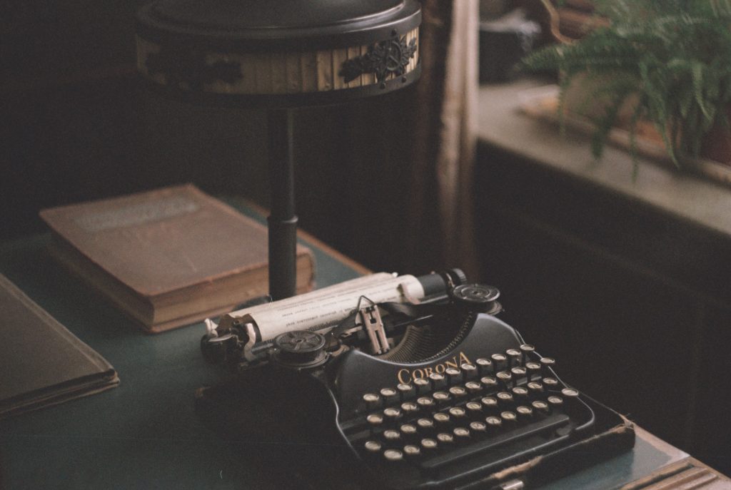 a table with books and an old typewriter with paper tucked in 